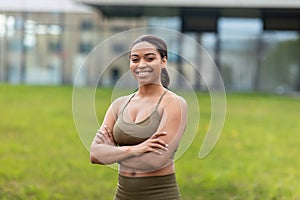 Portrait of happy young black woman in sports outfit posing at urban park