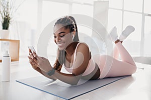 Portrait of happy young black woman using smartphone, listening to music on break from domestic training