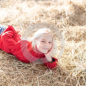 portrait happy of young blonde girl lying on haystack illuminated by bright sunshine. teenager on summer school vacation