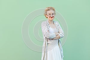 Portrait of happy young blonde woman in white shirt, skirt, and striped blouse with eyeglasses standing, crosed arms and looking