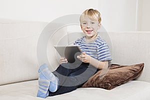 Portrait of happy young boy holding tablet PC on sofa