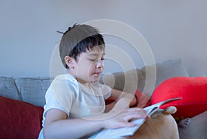 Portrait happy young boy sitting on sofa reading a schoolbook, Kid enjoy reading story relaxing at home, Home schooling concept