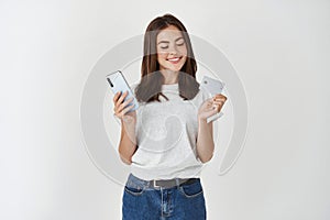 Portrait of a happy young brunette girl showing plastic credit card while holding mobile phone isolated over white