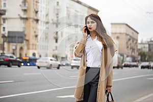 Portrait of happy young brunette woman in beige coat talking on