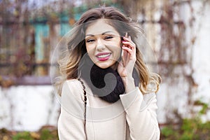 Portrait of happy young brunette woman in beige coat talking on