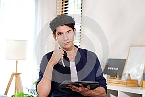Portrait of happy young business man owner holding digital tablet smiling and looking at camera while sitting at home office