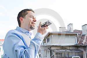 Portrait Happy Young Business Man using voice message recognition by his smartphone
