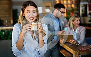 Portrait of happy young business woman drinking coffee in a break. In the background, her colleagues