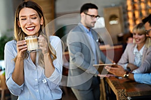 Portrait of happy young business woman drinking coffee in a break. In the background, her colleagues