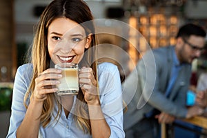 Portrait of happy young business woman drinking coffee in a break. In the background, her colleagues