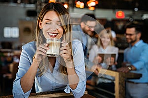 Portrait of happy young business woman drinking coffee in a break. In the background, her colleagues