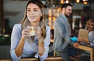 Portrait of happy young business woman drinking coffee in a break. In the background, her colleagues