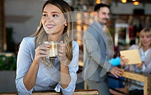 Portrait of happy young business woman drinking coffee in a break. In the background, her colleagues