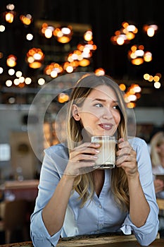 Portrait of happy young business woman drinking coffee in a break. In the background, her colleagues