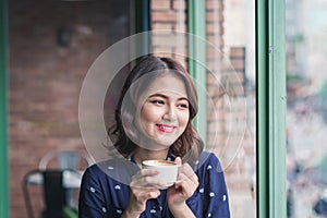 Portrait of happy young business woman with mug in hands drinking coffee in the morning at restaurant