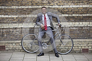 Portrait of a happy young businessman with bicycle against brick wall