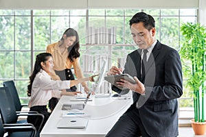 Portrait of happy young businessman looking at business document in tablet while his colleagues working in office background