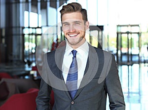 Portrait of happy young businessman standing in hotel lobby.