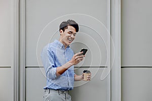 Portrait of a Happy Young Businessman Using Mobile Phone. Lifestyle of Modern People. Standing by the Wall