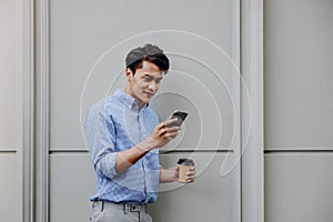 Portrait of a Happy Young Businessman Using Mobile Phone. Lifestyle of Modern People. Standing by the Wall