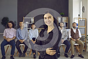 Portrait of happy young businesswoman standing in front of team of colleagues or employees