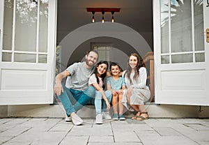 Portrait of a happy young caucasian family of four sitting at their front door smiling and looking at the camera. Two