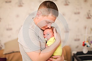 Portrait of happy young caucasian father holding his newborn baby indoor in selective focus