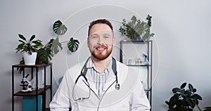 Portrait of happy young Caucasian medical consultant man in lab coat, stethoscope smiling at camera posing at workplace.