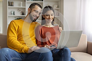 Portrait Of Happy Young Couple Browsing Internet On Laptop At Home