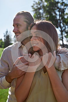 Portrait of happy young couple in casual wear smiling aside, posing together outdoors in summer park