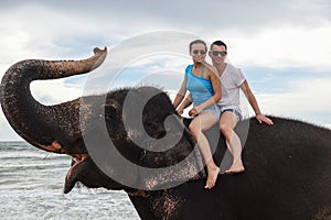 Portrait of a happy young couple on an elephant with trunk up on the background of a tropical ocean beach