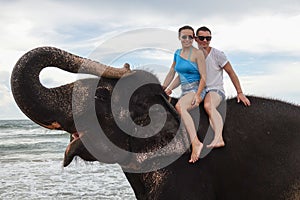 Portrait of a happy young couple on an elephant with trunk up on the background of a tropical ocean beach