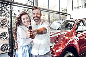 Portrait of a happy young couple hugging in a car salon showing car keys to a newly bought vehicle photo