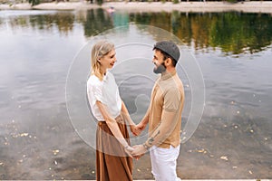 Portrait of happy young couple in love standing holding hands by beautiful city lake smiling looking at each other on