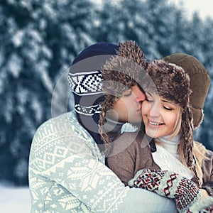 Portrait happy young couple in love at winter day, man gentle kissing woman wearing hat and knitted sweater