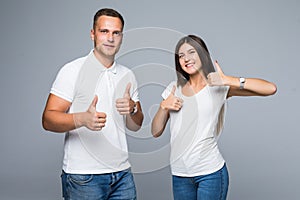 Portrait of happy young couple putting thumbs up on gray background