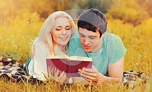 Portrait of happy young couple reading book together lying on the grass in the park