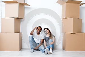 Portrait of happy young couple sitting on floor looking at camera and dreaming their new home and furnishing.