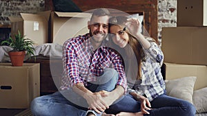 Portrait of happy young couple sitting together in new flat, holding keys and looking at camera. Nice loft style