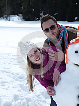 Portrait of happy young couple with snowman