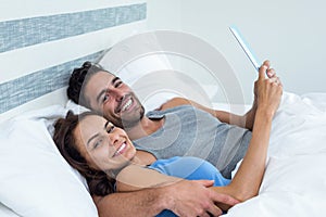 Portrait of happy young couple with tablet while lying on bed