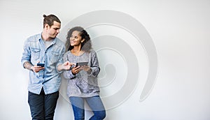 Portrait of happy young couple using smartphone standing isolated over white wall background.