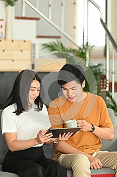 Portrait of happy young couple using tablet surfing on internet on couch.