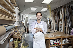 Portrait of a happy young craftsman standing with arms crossed in workshop