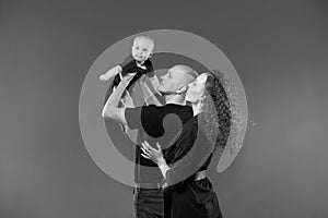 Portrait happy young family, dad holds his son in raised arms, mom stands next