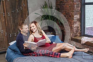 Portrait of happy young family have a rest in the bedroom, in sleepwear holding album are talking and smiling while spending time