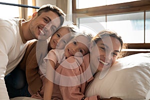 Portrait of happy young family with kids relaxing in bedroom