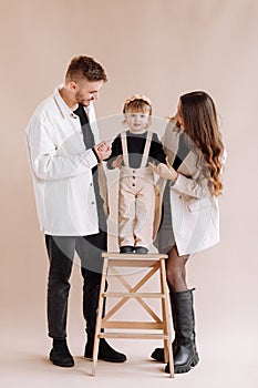 Portrait of a happy young family, with a little adorable daughter. parents holding a baby`s hands and hug her. child standing on