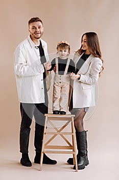 Portrait of a happy young family, with a little adorable daughter. parents holding a baby`s hands and hug her. child standing on