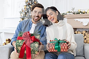 Portrait of a happy young family, a man and a woman sitting on the sofa at home, holding gift boxes, smiling and happy